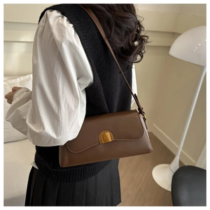 Close-up of a brown leather shoulder bag with gold buckle on a model in white shirt