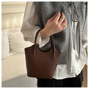 Detail of dark brown matte leather bucket bag with slim handles and precise stitching