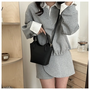 Minimalist black bucket bag shown with detachable strap in a cozy lifestyle setting