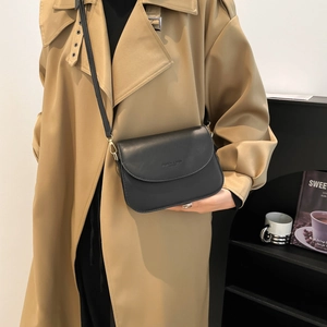 Minimalist black leather crossbody bag with flap and gold hardware on trench coat