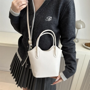 Minimalist white trapezoid handbag with top handle and adjustable strap in lifestyle setting