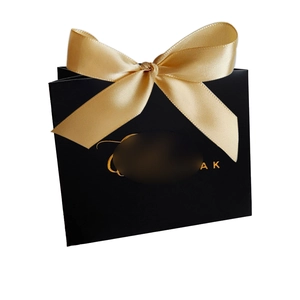 Close-up of matte black gift bag featuring a wide gold satin bow and elegant gold lettering
