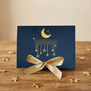 Close-up of luxury navy gift box with gold foil moon, stars, and champagne satin ribbon bow