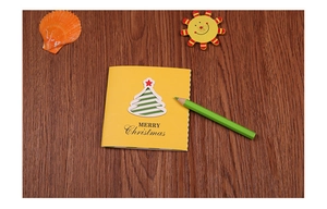 Macro detail of square yellow Christmas card with cutout tree on wooden surface