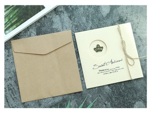 Detail of vintage kraft envelope with handmade card featuring a bronze crown charm and twine