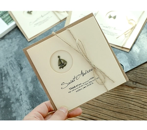Close-up of vintage kraft greeting card with bronze sailboat charm and jute twine