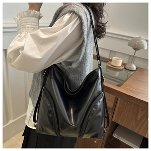 Close-up of a black minimalist leather tote bag showing smooth texture and side zipper detail