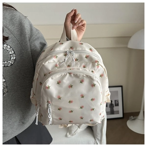 Detail eines Mini-Rucksacks in Cremeweiß mit rosa Rosenmuster und vorderer Reißverschlusstasche