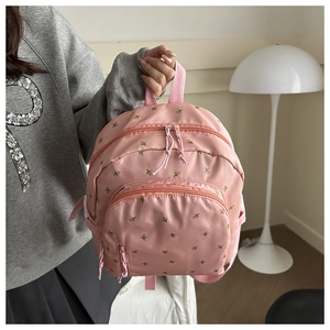 Detail eines hellrosa Mini-Rucksacks mit Blumenstickerei und pinken Reißverschlusszügen