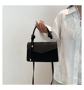 Detail of black woven shoulder bag with knot handle and gold hardware on white lace top