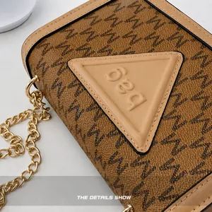 Nahaufnahme der braunen Monogramm-Umhängetasche mit goldener Kette und Letter-Dreiecksplakette