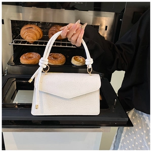 Details einer weißen Handtasche mit Blumenprägung, goldenem Verschluss und Quastenakzent