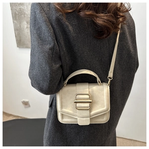 Détail d'un sac bandoulière beige mat avec une boucle carrée dorée sur un manteau gris