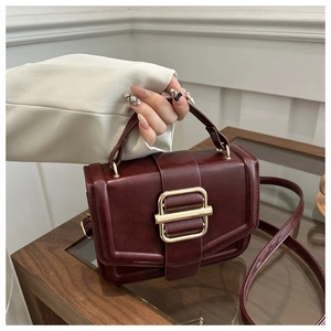 Détail d'un sac à main bordeaux avec une grande boucle dorée et une poignée chic