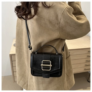 Détail d'un sac bandoulière noir avec boucle dorée porté sur une veste en daim