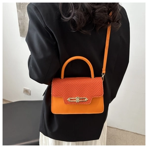 Detail showing the orange crossbody box bag with woven texture and gold metal buckle