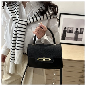 Detail of a black leather box bag featuring a textured flap and elegant gold metal clasp