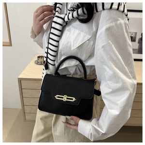 Detail of black box bag showing textured flap and golden metal clasp on a white shirt