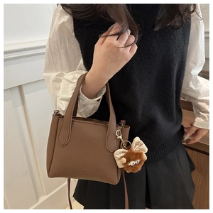 Detail of brown litchi pattern leather bucket bag with cute plush pendant and strap