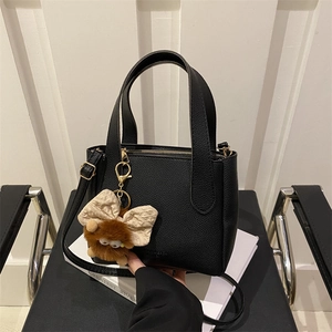 Minimalist black bucket shoulder bag with plush monster charm and lychee texture