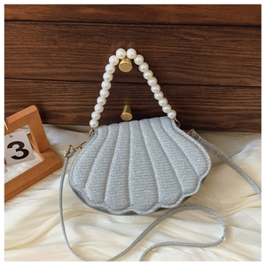 Detail of shell-shaped handbag featuring glitter fabric and large white pearl handle