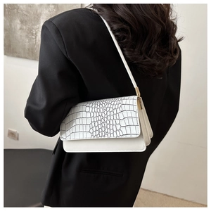 Detail of white baguette bag with crocodile texture flap and gold hardware accents