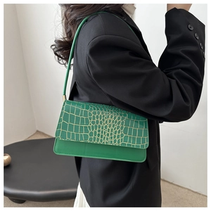 Close-up of green crocodile embossed baguette bag worn on shoulder by a model