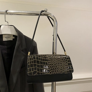 Detail of black crocodile texture shoulder bag featuring gold hardware on clothing rack