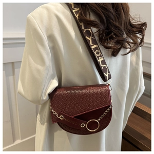Détail d'un sac selle bordeaux avec rabat gaufré tressé et chaîne dorée élégante