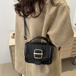 Sac bandoulière minimaliste en cuir noir mat avec boucle dorée porté par un mannequin