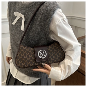 Detail of vintage monogram shoulder bag featuring a silver M logo and brown leather strap