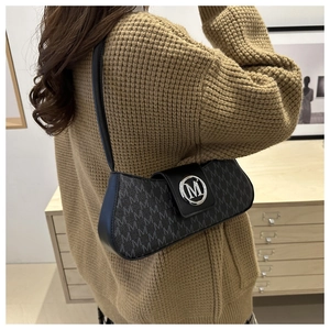 Detail of black underarm bag with letter M print and silver round logo worn by model