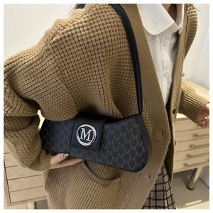 Detail of black underarm bag with grey M-letter pattern and silver metal buckle