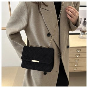 Detail of black crossbody bag with V-quilted texture and gold chain strap on model