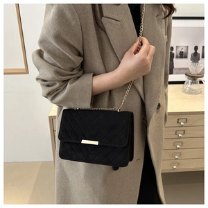Detail of black V-quilted crossbody bag with gold chain strap on a wool coat outfit