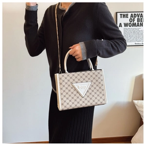 Detail of monogram tote bag with white triangle logo and patterned fabric shoulder strap
