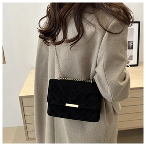 Close-up of black quilted chain bag with V-shaped stitching and gold metal bar detail