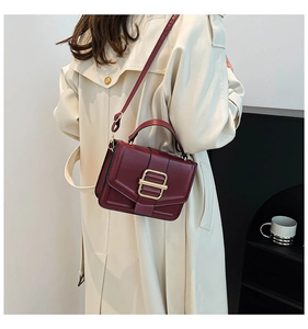 Detail of burgundy leather handbag with large gold buckle on model with beige coat