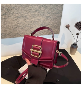 Detail of burgundy PU leather crossbody bag with elegant gold rectangular metal buckle