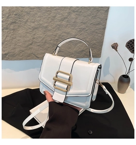 Detail of white leather handbag with gold rectangular buckle and adjustable shoulder strap