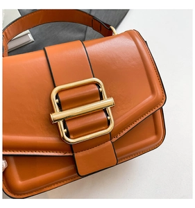 Close-up of orange-brown crossbody bag featuring a large gold buckle and fine stitching