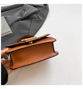 Detail view of brown leather crossbody bag with gold lock and black edge finish