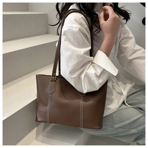Detail view of large dark brown tote bag with white contrast stitching and gold buckles