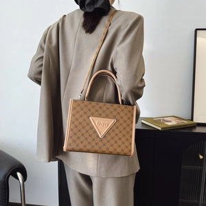 Brown monogram tote bag with letter detail, worn as a crossbody for daily commute style