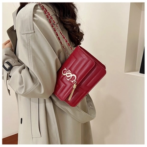 Detail of red faux leather crossbody bag with metal logo, tassel, and chain strap