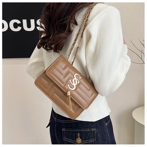 Detail of brown quilted leather crossbody bag with gold chain strap and tassel charm