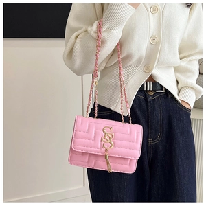Detail of pink quilted crossbody bag with golden chain strap and tassel on white sweater