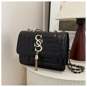 Detail of black quilted leather handbag with gold metal logo and tassel on a display stand