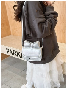 Primer plano de un mini bolso plateado para niñas con un lazo grande y acabado metálico