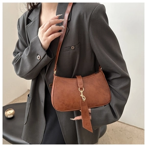 Detail view of brown leather crescent bag featuring a metallic hook and vintage texture